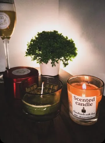 Scented candle jar glowing beside a small plant and wine glass