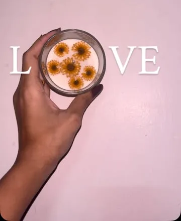 Hand holding a jar candle with pressed orange flowers