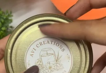 Gold tin candle lid printed with the Avi Creations logo